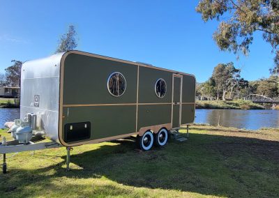 Stylish green caravan with a silver top parked by the lake at Stawell Hotel Motel Accommodation, surrounded by trees and showcasing a tranquil outdoor setting