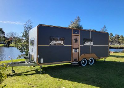 Stylish black caravan with a silver top parked by the lake at Stawell Hotel Motel Accommodation, surrounded by trees and showcasing a tranquil outdoor setting