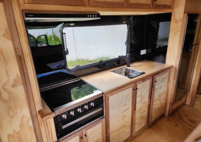 Modern caravan kitchen with a cooktop, sink, and ample storage cabinets, illuminated by natural light through a large window, offering a functional space for cooking at Stawell Hotel Motel Accommodation