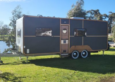 Modern green caravan parked by the lake at Stawell Hotel Motel Accommodation, featuring a stylish design with dark green and wood paneling against a clear blue sky
