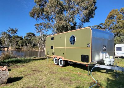 Stylish green caravan with a silver top parked by the lake at Stawell Hotel Motel Accommodation, surrounded by trees and showcasing a tranquil outdoor setting