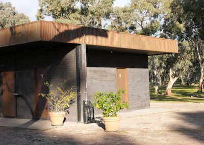 Exterior view of ensuite accommodation at Stawell Hotel Motel, featuring two separate doors numbered 76 and 79, surrounded by lush greenery and potted plants, with a modern, minimalist design set against a backdrop of tall trees