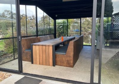Interior view of the dining area at Stawell Hotel Motel, showcasing a wooden table with bench seating, surrounded by glass walls that provide a scenic view of the outdoors and nearby water