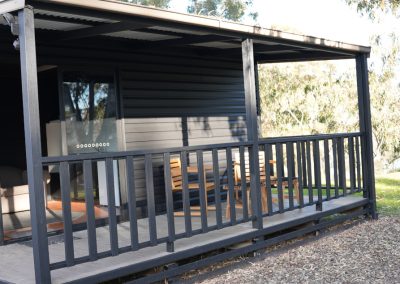 Exterior view of a Cabin at Stawell Hotel Motel, featuring a covered porch with a wooden railing and seating area, showcasing a modern design against a backdrop of lush greenery