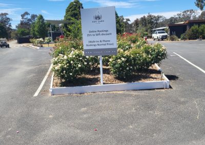 Signage at Stawell Hotel Motel Accommodation advertising online booking discounts of 25% to 50%. The sign is surrounded by well-maintained flower beds and greenery, with a clear blue sky in the background. Nearby parking spaces are visible, enhancing the welcoming atmosphere of the motel
