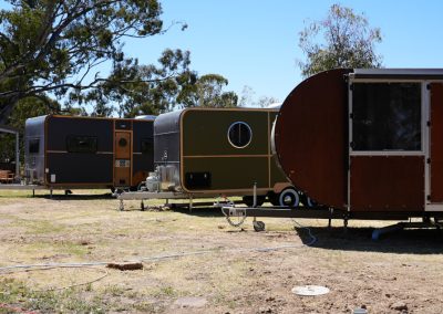 View of unique Hammervans at Stawell Hotel Motel Accommodation, showcasing a variety of modern trailer designs with distinctive rounded and rectangular shapes. Set against a backdrop of greenery, these stylish accommodations provide a contemporary option for guests looking for a unique stay in a scenic environment