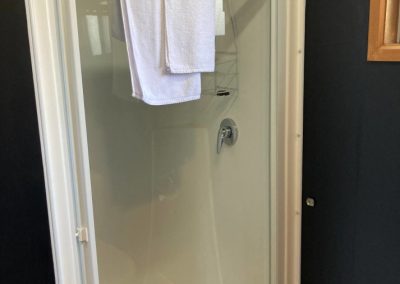 Interior view of the shower in Cabin 32 at Stawell Hotel Motel Accommodation, featuring a glass shower enclosure with a chrome showerhead. White towels are neatly hung on a rack, and the clean, modern design is enhanced by light-colored walls and a window that provides natural light