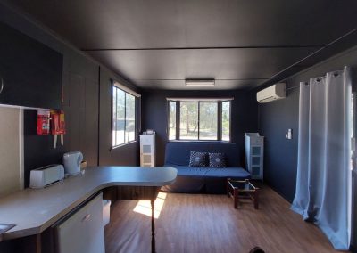 Open-plan living area in a modern cabin with a kitchenette, sofa, and large windows allowing natural light, perfect for relaxing at Stawell Hotel Motel Accommodation