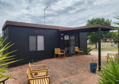 Exterior of a black cabin with a brick patio, outdoor seating, and a covered entrance at Stawell Hotel Motel Accommodation