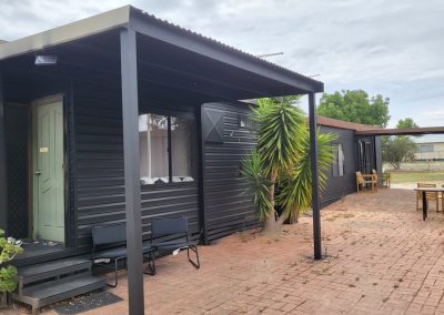 Modern black cabin with a covered entrance, brick patio, and surrounding greenery at Stawell Hotel Motel Accommodation