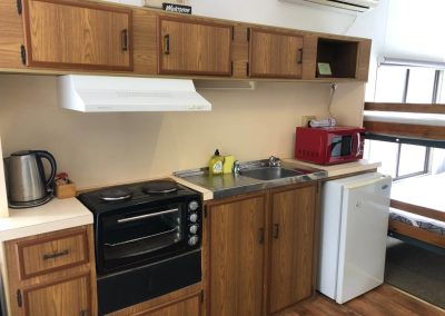 Fully equipped cabin kitchenette with a mini-fridge, microwave, oven, and wooden cabinetry at Stawell Hotel Motel Accommodation