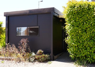 Private black cabin surrounded by lush greenery and garden plants, offering a peaceful retreat at Stawell Hotel Motel Accommodation