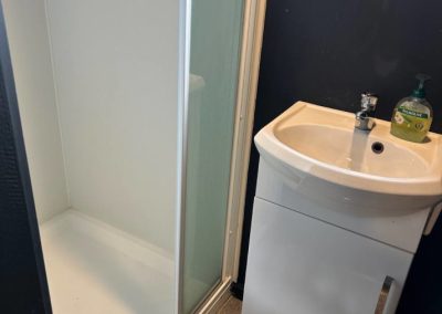 Modern bathroom in Cabin 30 showcasing a clean shower area with a glass door and a sleek white sink with storage underneath. The minimalist design is enhanced by dark walls and a large window that allows natural light to fill the space at Stawell Hotel Motel Accommodation