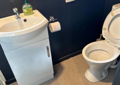 Compact bathroom in Cabin 30 featuring a modern white sink with a sleek design, complemented by a nearby toilet. The space is enhanced by dark walls and a polished floor, with a bottle of hand soap on the sink for convenience at Stawell Hotel Motel Accommodation