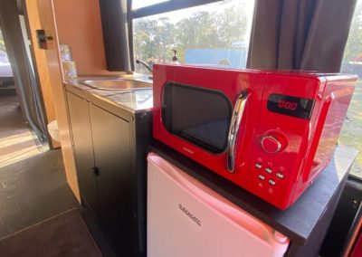 Compact kitchenette in a converted bus accommodation, featuring a red microwave, mini-fridge, and sink at Stawell Hotel Motel Accommodation