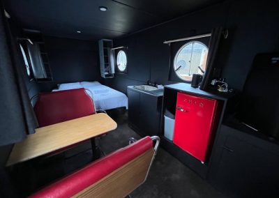 Interior of a modern, compact caravan with round windows, featuring a cozy bed, small kitchenette, and red retro-style refrigerator at Stawell Hotel Motel Accommodation