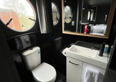 Modern black-themed bathroom with round porthole windows, a white vanity, and toilet inside a caravan at Stawell Hotel Motel Accommodation