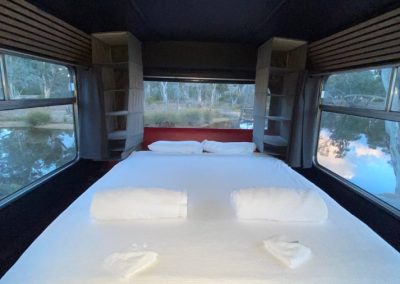 Spacious modern bedroom inside a caravan at Stawell Hotel Motel Accommodation, featuring a large white bed with scenic window views of trees and water