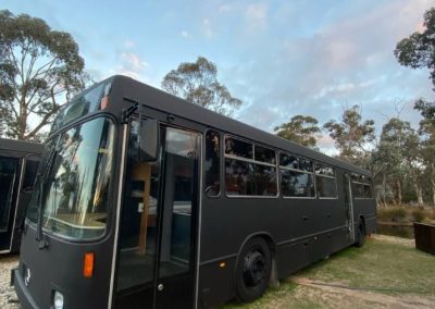 Exterior view of a converted black bus at Stawell Hotel Motel Accommodation, set amidst natural surroundings with trees and a grassy area, providing a unique lodging experience