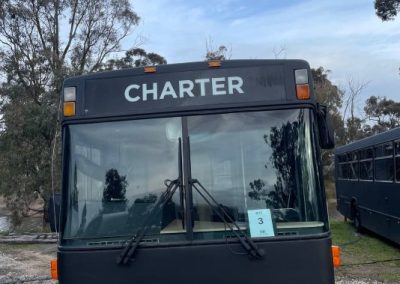 Front view of a black converted charter bus, labeled 'Bus 3,' parked on a gravel surface with trees in the background, offering a unique accommodation option at Stawell Hotel Motel Accommodation